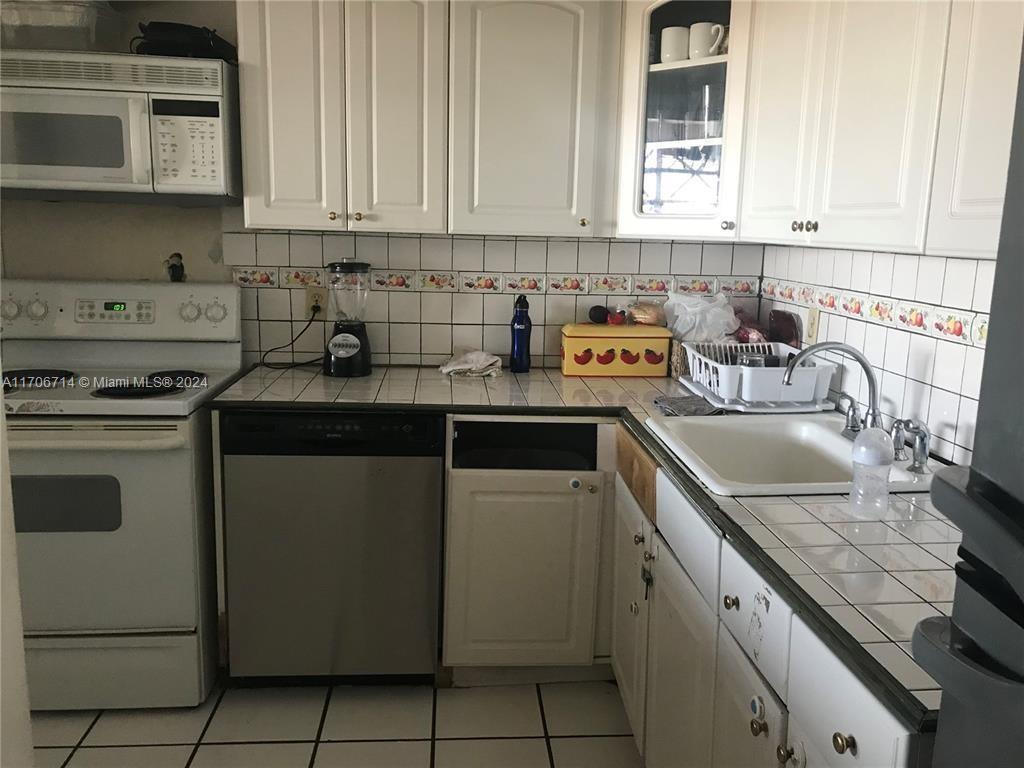 kitchen featuring light tile patterned floors, white appliances, white cabinetry, and sink