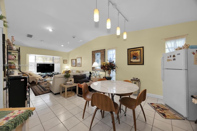 tiled dining room featuring rail lighting and lofted ceiling