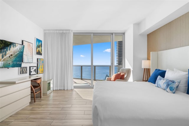 bedroom featuring access to outside, light wood-type flooring, a water view, and a wall of windows