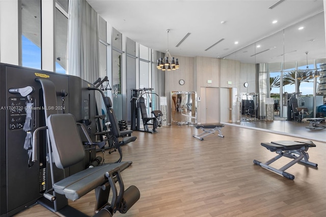 exercise room with light hardwood / wood-style floors, floor to ceiling windows, a high ceiling, and a chandelier