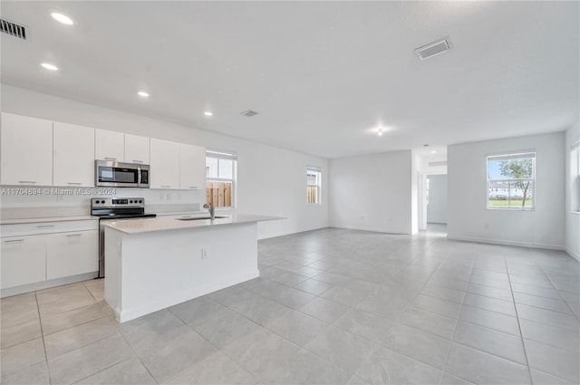 kitchen with sink, stainless steel appliances, light tile patterned floors, a center island with sink, and white cabinets