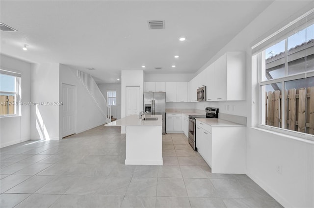 kitchen featuring sink, stainless steel appliances, white cabinets, an island with sink, and light tile patterned flooring