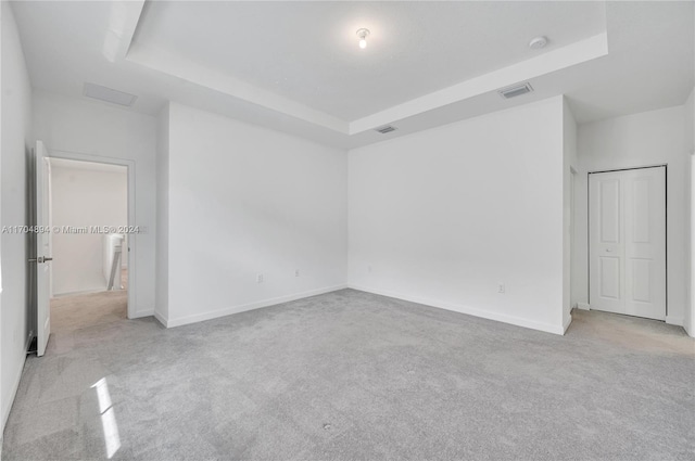 empty room with a raised ceiling and light carpet