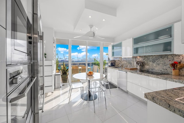 kitchen featuring decorative backsplash, light stone countertops, black electric cooktop, dishwasher, and white cabinetry