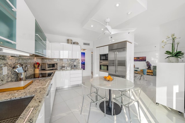 kitchen with tasteful backsplash, light stone counters, black appliances, white cabinets, and light tile patterned flooring