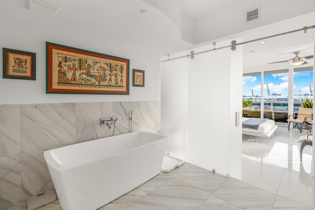 bathroom featuring a tub, ceiling fan, a water view, and tile walls