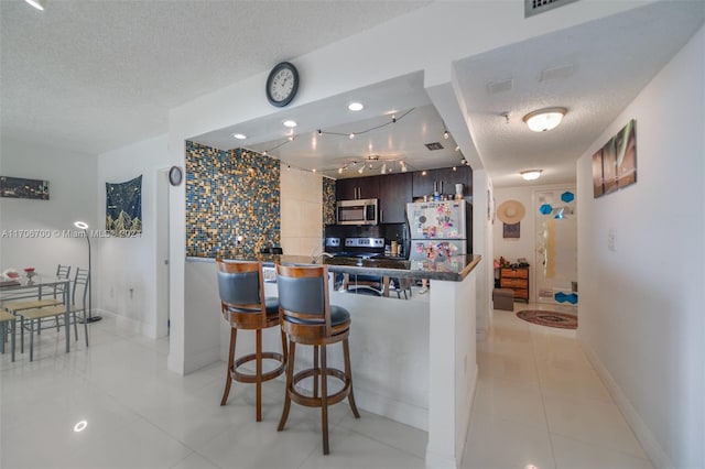 kitchen featuring light tile patterned floors, a textured ceiling, appliances with stainless steel finishes, dark brown cabinets, and kitchen peninsula