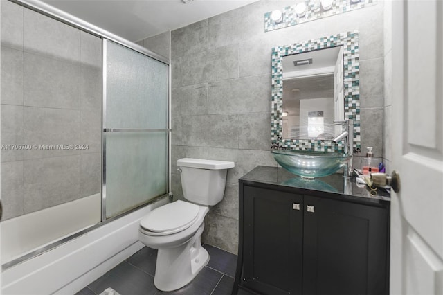 full bathroom with vanity, combined bath / shower with glass door, tile patterned flooring, toilet, and tile walls