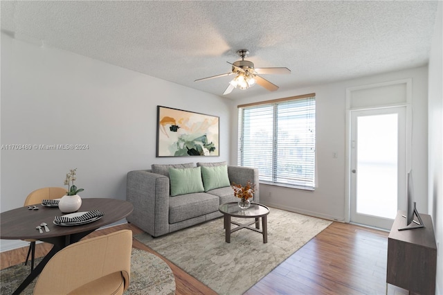 living room featuring ceiling fan, light hardwood / wood-style flooring, and a textured ceiling