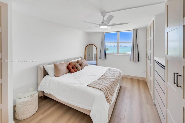 bedroom featuring ceiling fan, a water view, and light hardwood / wood-style floors