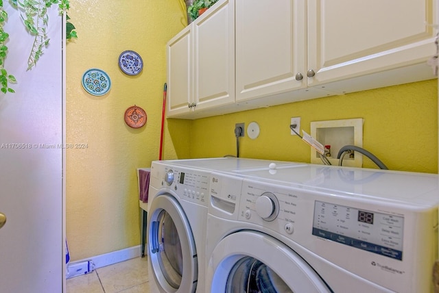 clothes washing area with washing machine and dryer, light tile patterned floors, and cabinets