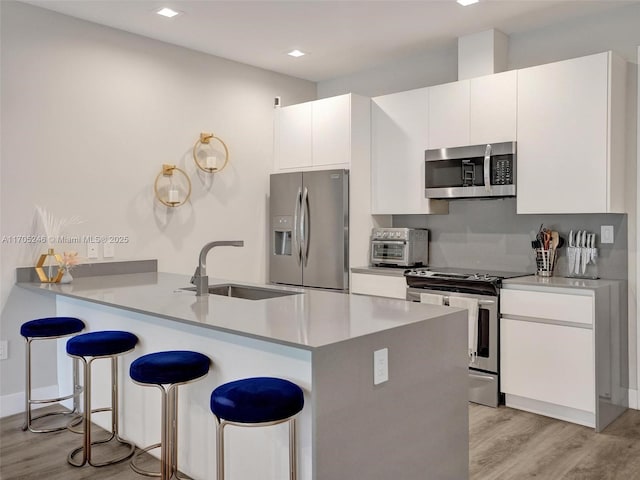 kitchen featuring a kitchen bar, sink, kitchen peninsula, stainless steel appliances, and white cabinets