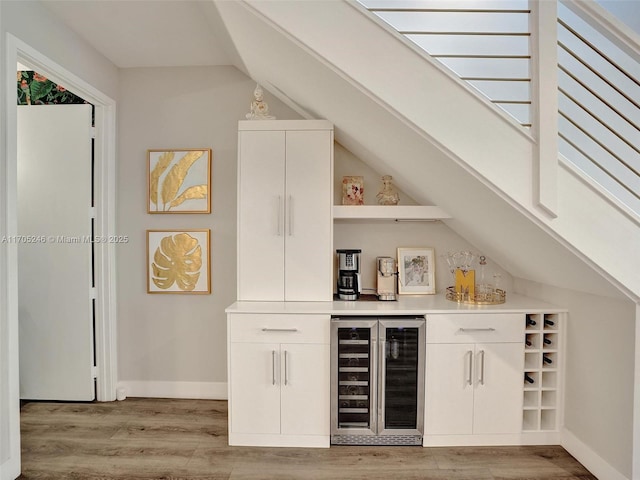 bar with lofted ceiling, beverage cooler, light hardwood / wood-style floors, and white cabinets