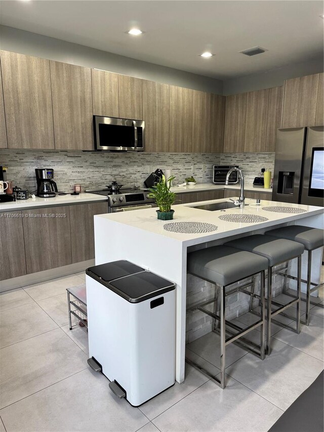 kitchen with appliances with stainless steel finishes, a breakfast bar area, a center island with sink, and light tile patterned floors