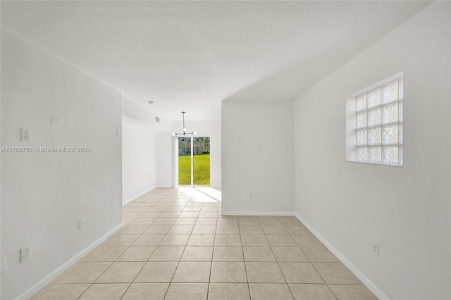 tiled spare room featuring a textured ceiling and an inviting chandelier