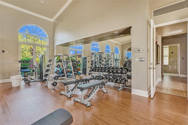 exercise room featuring hardwood / wood-style floors, crown molding, and high vaulted ceiling