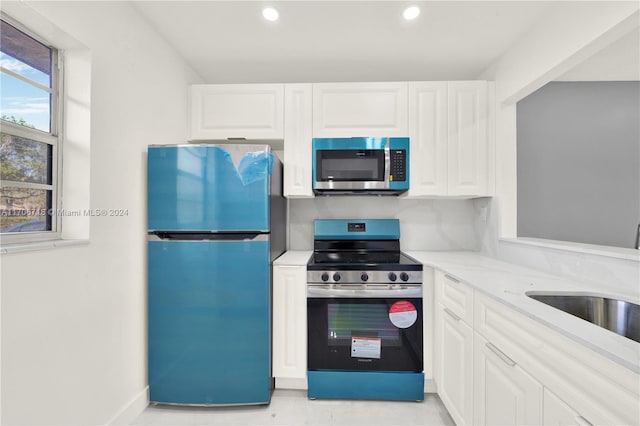 kitchen with white cabinets, stainless steel appliances, light stone counters, and sink