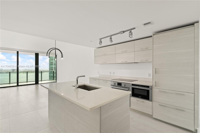 kitchen with black electric cooktop, stainless steel oven, sink, and an island with sink