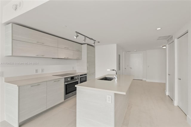 kitchen featuring black electric cooktop, an island with sink, oven, and sink