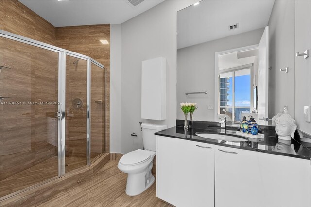 bathroom with wood-type flooring, vanity, toilet, and a shower with shower door