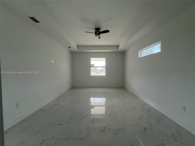 empty room with ceiling fan and a raised ceiling