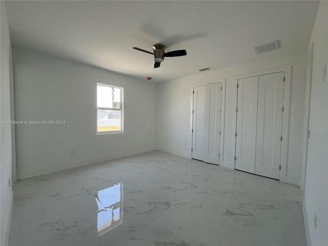 unfurnished bedroom featuring ceiling fan and two closets