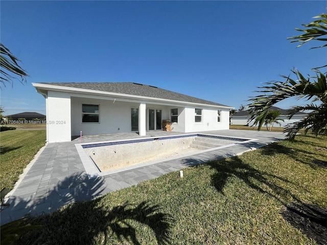 rear view of property featuring a yard, a patio, and an empty pool