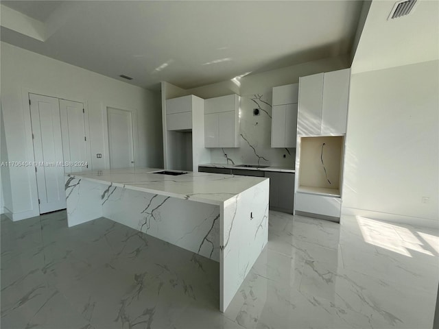 kitchen featuring white cabinetry, light stone countertops, sink, stainless steel stovetop, and a kitchen island