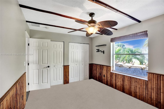 unfurnished bedroom featuring carpet, wood walls, ceiling fan, a textured ceiling, and multiple closets