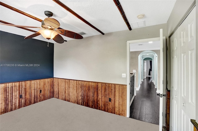 empty room featuring a textured ceiling, ceiling fan, dark wood-type flooring, and wood walls