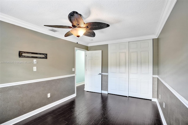 unfurnished bedroom featuring ceiling fan, dark wood-type flooring, crown molding, a textured ceiling, and a closet