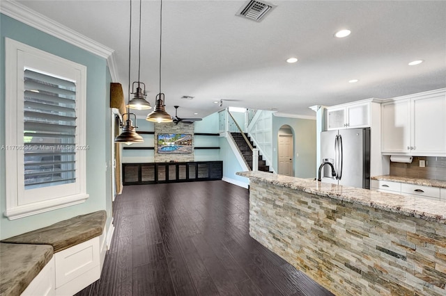 kitchen with dark wood-type flooring, hanging light fixtures, stainless steel fridge, light stone countertops, and white cabinetry