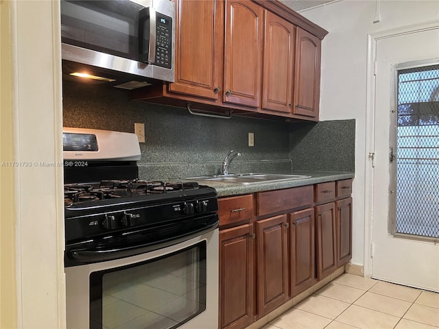 kitchen featuring backsplash, sink, light tile patterned flooring, and range with gas stovetop