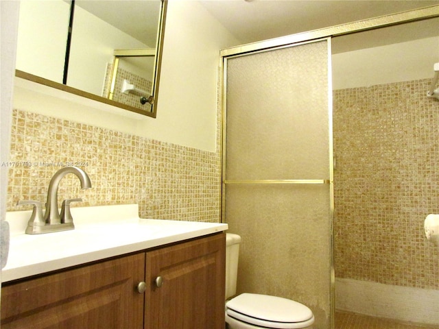 bathroom with vanity, decorative backsplash, toilet, tile walls, and a shower with shower door