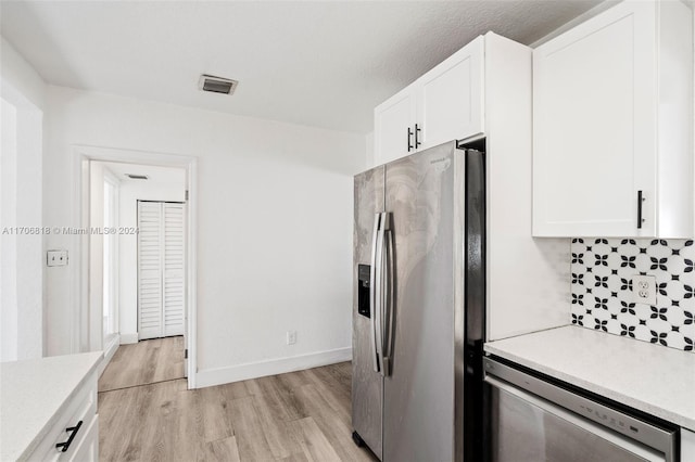 kitchen with backsplash, white cabinets, light wood-type flooring, and appliances with stainless steel finishes