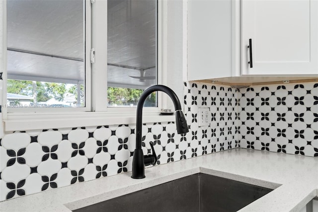 details with decorative backsplash, white cabinetry, light stone countertops, and sink