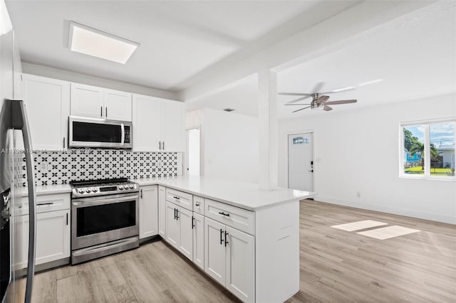 kitchen with white cabinetry, light hardwood / wood-style flooring, backsplash, kitchen peninsula, and appliances with stainless steel finishes