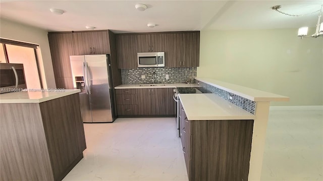 kitchen with appliances with stainless steel finishes, sink, backsplash, hanging light fixtures, and dark brown cabinetry