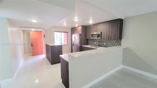 kitchen featuring decorative backsplash, stainless steel appliances, kitchen peninsula, and dark brown cabinets