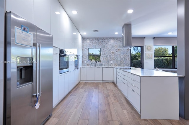 kitchen featuring kitchen peninsula, decorative backsplash, light hardwood / wood-style floors, white cabinetry, and stainless steel appliances