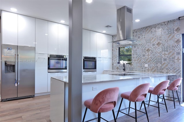 kitchen with decorative backsplash, a kitchen breakfast bar, island exhaust hood, stainless steel built in refrigerator, and white cabinets