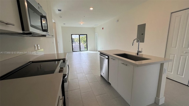 kitchen with electric panel, white cabinets, a center island with sink, sink, and appliances with stainless steel finishes