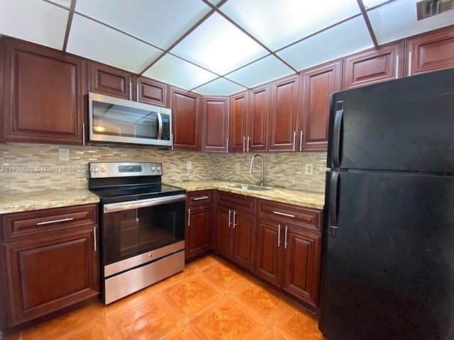 kitchen with appliances with stainless steel finishes, a paneled ceiling, tasteful backsplash, light stone counters, and sink