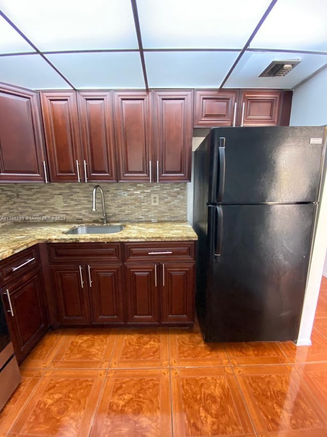 kitchen with light stone countertops, sink, a paneled ceiling, decorative backsplash, and black refrigerator