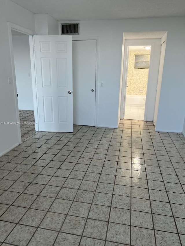 unfurnished bedroom with ensuite bathroom, a closet, and light tile patterned flooring