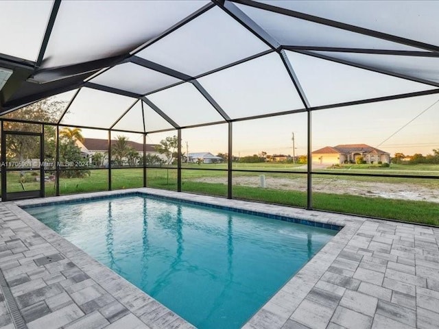 pool at dusk with glass enclosure, a yard, and a patio