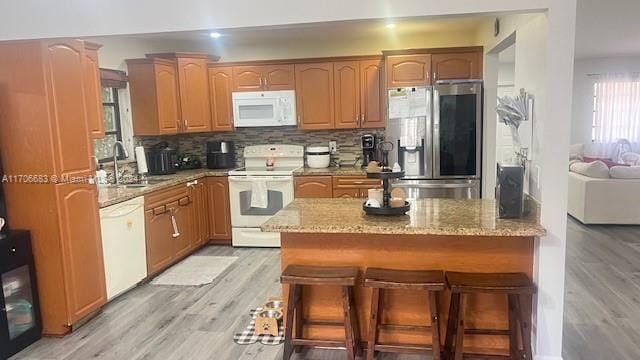 kitchen with a kitchen breakfast bar, light wood-type flooring, backsplash, white appliances, and sink