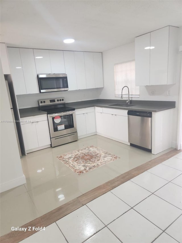 kitchen featuring appliances with stainless steel finishes, light tile patterned floors, white cabinetry, and sink