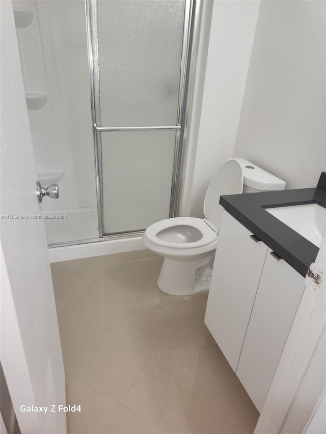 bathroom featuring tile patterned floors, vanity, a shower with shower door, and toilet