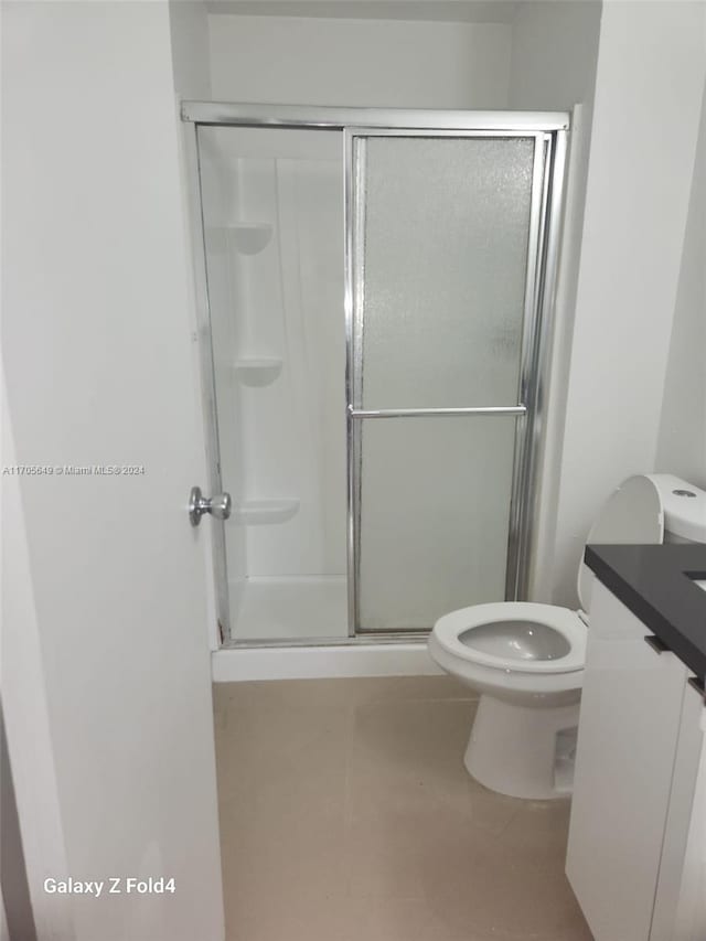 bathroom featuring tile patterned flooring, vanity, an enclosed shower, and toilet